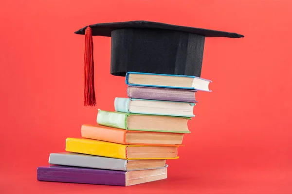 Casquette académique avec pompon et livres lumineux sur surface rouge — Photo de stock