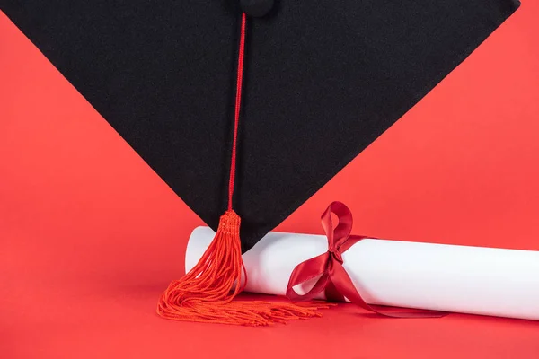 Tampa acadêmica com borla e diploma com fita na superfície vermelha — Fotografia de Stock