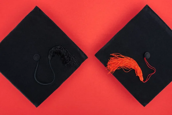 Vista superior de gorras académicas negras con borlas en superficie roja - foto de stock