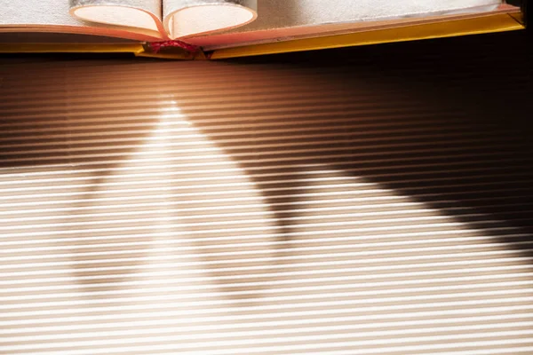 Open book with folded pages on textured surface with heart-shaped shadow — Stock Photo