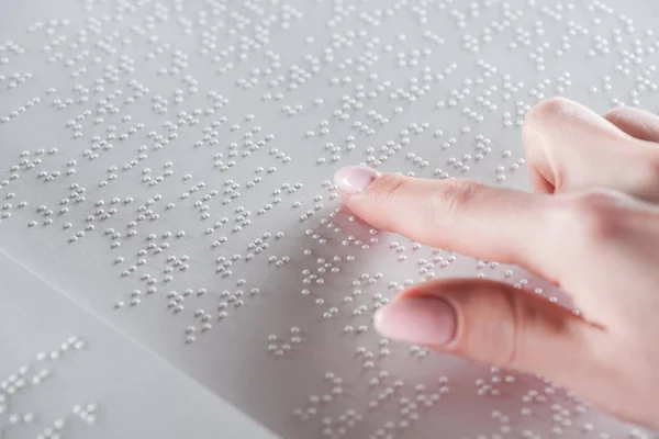 Partial view of young woman reading braille text on white paper — Stock Photo