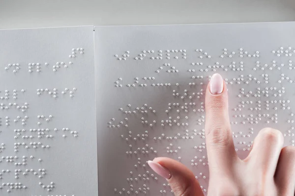 Top view of young woman reading braille text on white paper — Stock Photo