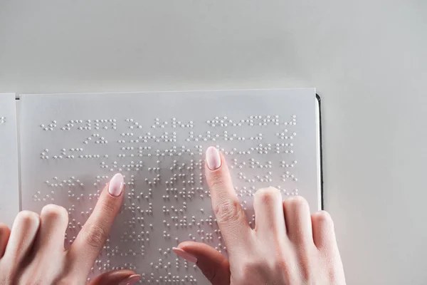 Vista superior de la joven leyendo texto braille sobre papel blanco aislado sobre gris - foto de stock