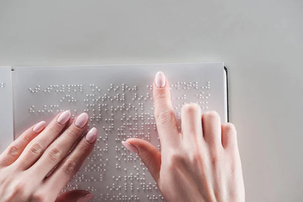 Vista superior de la joven leyendo texto braille sobre papel blanco aislado sobre gris - foto de stock