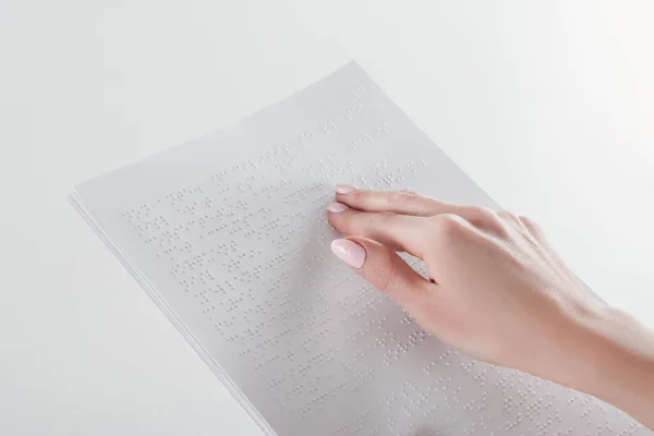 Vista recortada de la mujer joven leyendo texto braille con la mano en el papel blanco - foto de stock