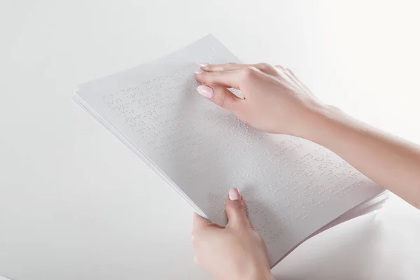 Vista recortada de la mujer joven leyendo texto braille con la mano en el papel blanco - foto de stock