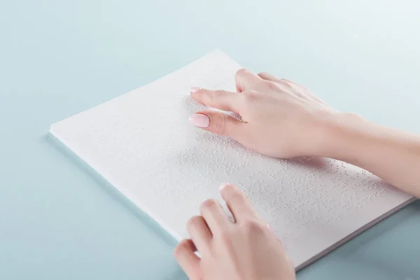 Vista ritagliata di giovane donna che legge testo in braille su carta isolata su blu — Foto stock