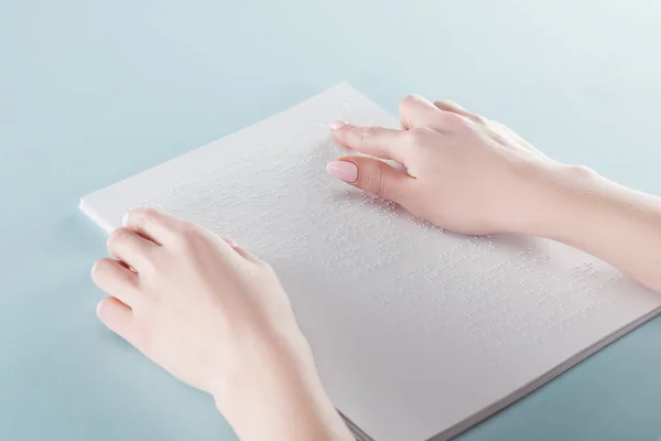 Cropped view of young woman reading braille text on paper isolated on blue — Stock Photo