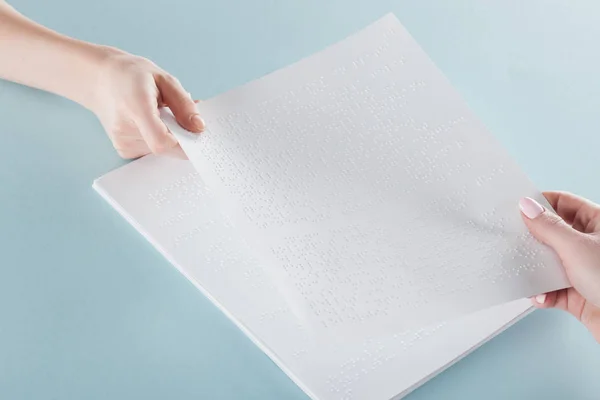 Vista cortada de mulheres jovens segurando papel com texto braille isolado em azul — Fotografia de Stock