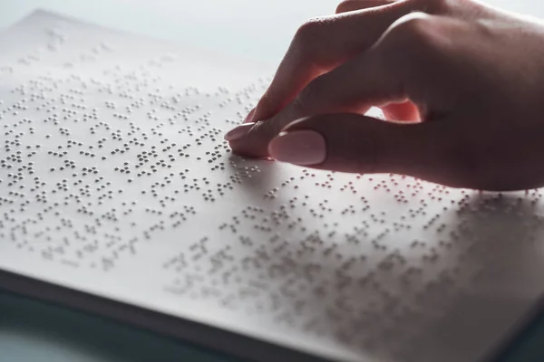 Cropped view of young woman reading braille text on white paper — Stock Photo