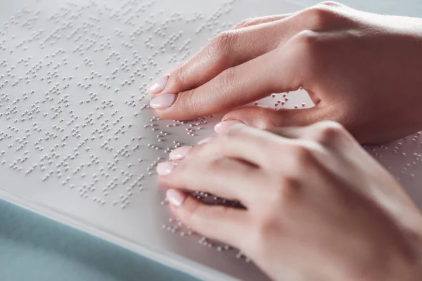 Vista ritagliata di ragazza che legge il testo in braille con le mani su carta bianca — Foto stock