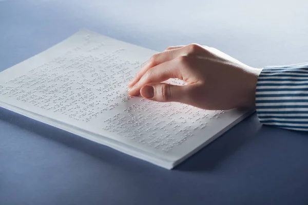 Vista ritagliata di giovane donna che legge il testo in braille con mano sul blu — Foto stock