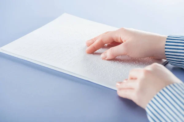 Cropped view of young woman reading braille text with hand isolated on violet — Stock Photo