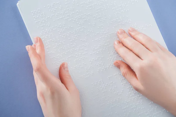 Partial view of young woman reading braille text with hand isolated on violet — Stock Photo