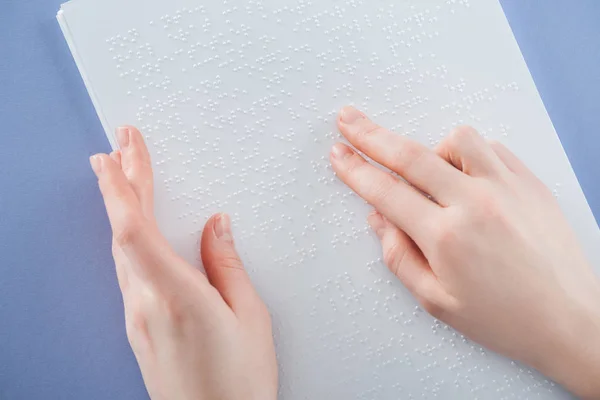 Partial view of young woman reading braille text with hand isolated on violet — Stock Photo