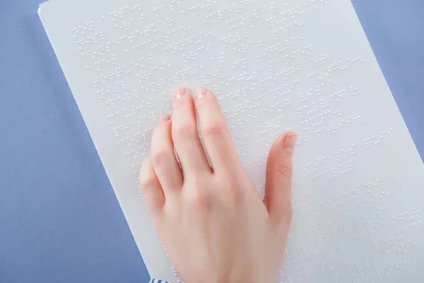 Top view of young woman reading braille text with hand isolated on violet — стоковое фото