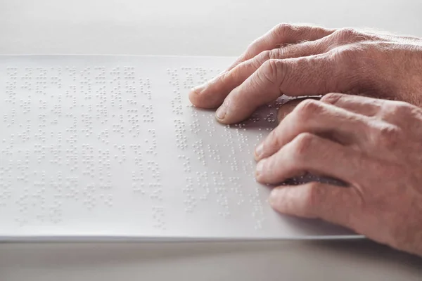 Vista recortada del hombre mayor leyendo texto braille aislado en gris - foto de stock