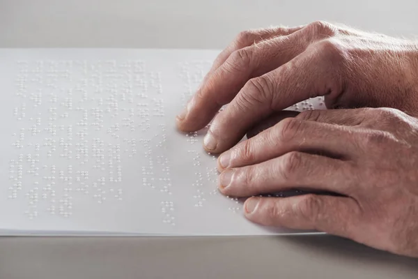 Partial view of senior man reading braille text isolated on grey — Stock Photo