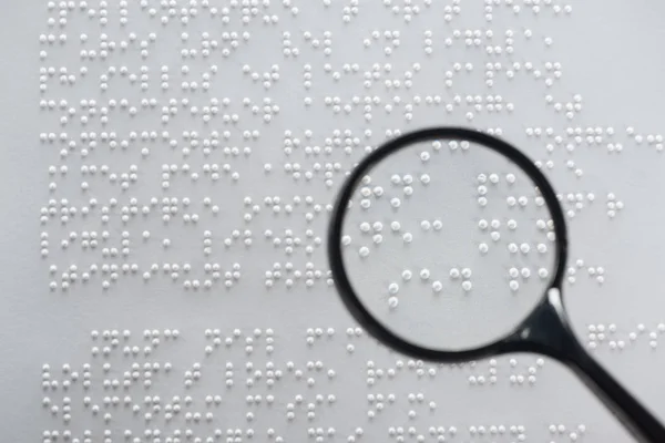 Top view of braille text on white paper with magnifying glass — Stock Photo