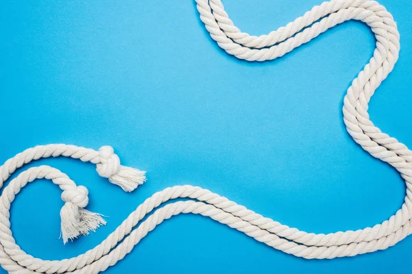 Long white waved ropes with knots isolated on blue — Stock Photo