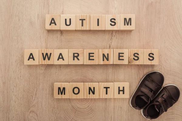 Top view of autism awareness month words made of wooden blocks near brown children sneakers — Stock Photo
