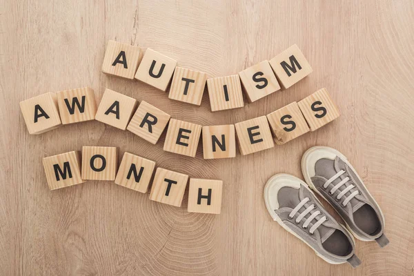 Vista superior del autismo mes de conciencia palabras hechas de bloques de madera cerca de las zapatillas de deporte grises para niños - foto de stock