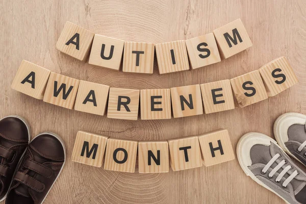 Vista superior da consciência autismo mês palavras feitas de blocos de madeira perto de marrom e cinza crianças sapatilhas — Fotografia de Stock