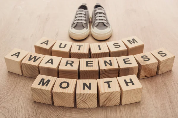 Autism awareness month words made of wooden blocks near grey children sneakers — Stock Photo