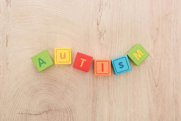 Vista dall'alto di scritte autistiche ondulate fatte di cubi multicolori su tavolo di legno — Foto stock