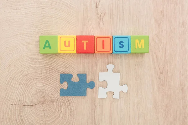 Vista superior de letras autistas hechas de cubos multicolores cerca de piezas de rompecabezas en mesa de madera - foto de stock