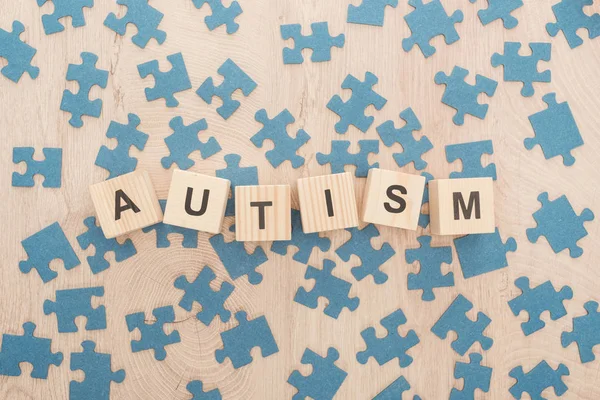 Top view of autism lettering made of wooden cubes among blue puzzle pieces on wooden table — Stock Photo