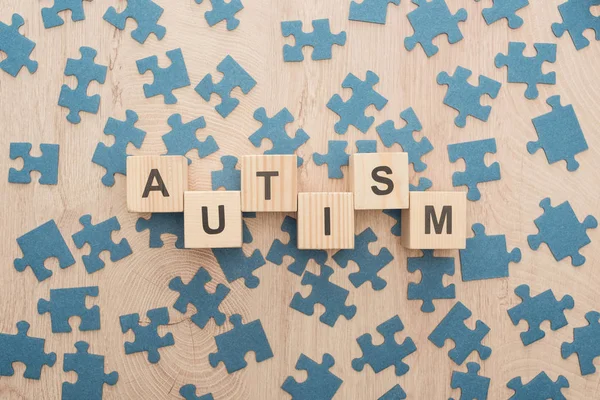 Top view of autism lettering made of wooden blocks among puzzle pieces on wooden table — Stock Photo
