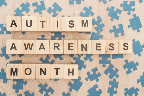 Vista dall'alto di autismo consapevolezza mese lettering fatto di blocchi di legno tra pezzi di puzzle sul tavolo di legno — Foto stock