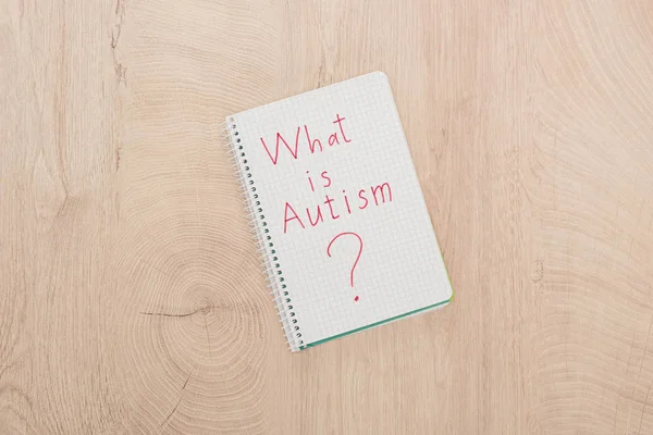 Vista superior de lo que es cuestión de autismo escrito en cuaderno sobre mesa de madera - foto de stock