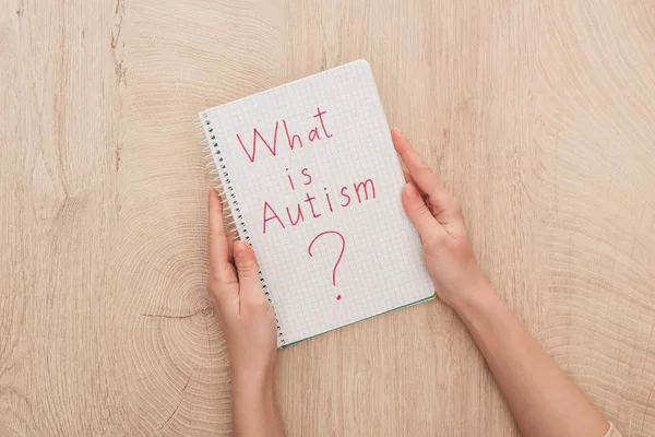 Vista recortada de la mujer que sostiene el cuaderno con lo que es cuestión de autismo en la mesa de madera - foto de stock