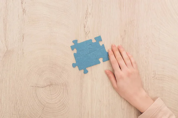 Ausgeschnittene Ansicht einer weiblichen Hand in der Nähe blauer Puzzles auf Holztisch — Stockfoto