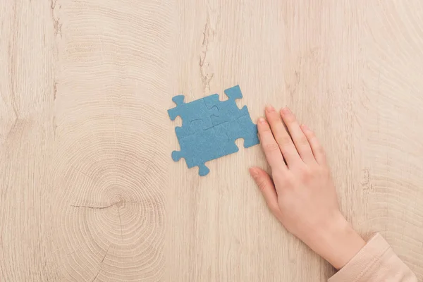 Vista recortada de la mano femenina cerca de rompecabezas azules en la mesa de madera - foto de stock