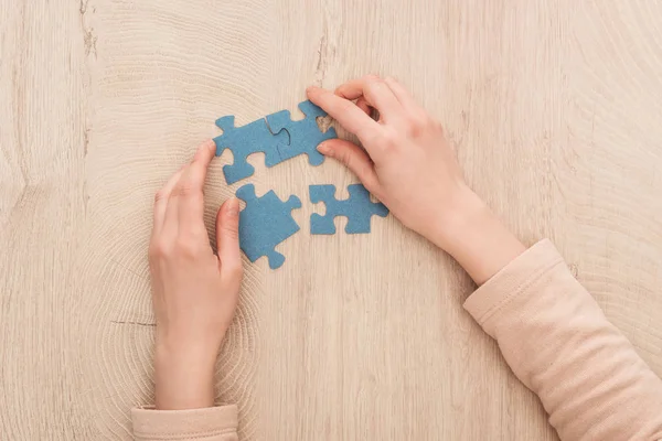 Ausgeschnittene Ansicht weiblicher Hände mit blauen Puzzles auf Holztisch — Stockfoto
