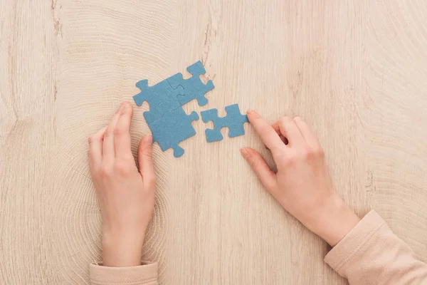 Частковий вигляд жіночих рук з синіми головоломками на дерев'яному столі — Stock Photo