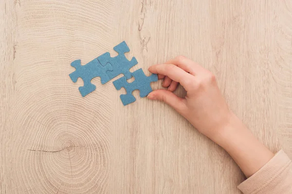 Vista parziale della mano femminile con puzzle blu sul tavolo di legno — Foto stock