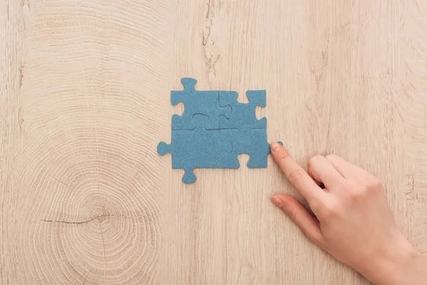 Ausgeschnittene Ansicht einer weiblichen Hand, die mit dem Finger auf blaue Puzzleteile zeigt, die auf einem Holztisch verbunden sind — Stockfoto