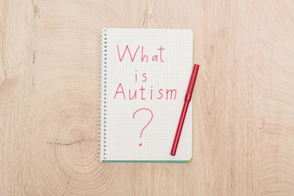 Вид зверху на червоний маркер і питання аутизму, написане в блокноті на дерев'яному столі — стокове фото