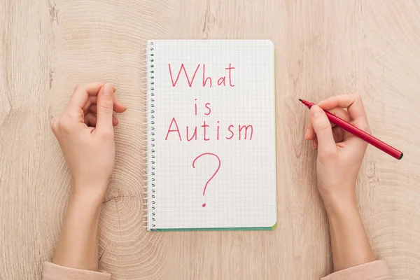Cropped view of woman holding marker near notebook with what is autism question on wooden table — Stock Photo