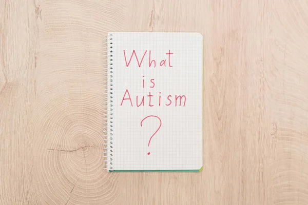 Вид зверху на червоне питання аутизму, написане в блокноті на дерев'яному столі — стокове фото