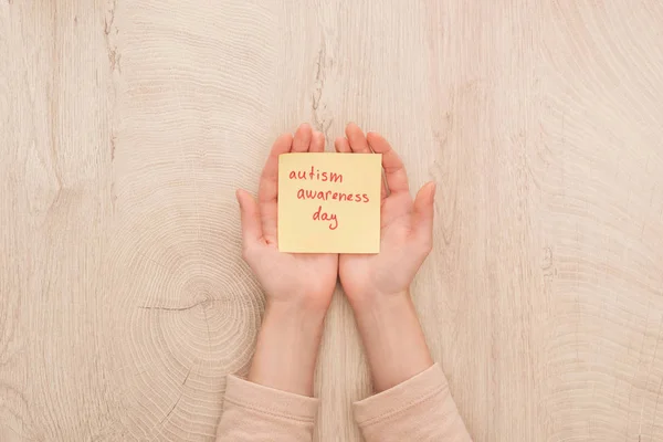 Cropped view of female hands and sticky note with red autism awareness day handwritten lettering — Stock Photo