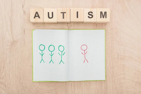 Vista superior del cuaderno abierto con diferentes seres humanos dibujados cerca de cubos de madera con letras de autismo - foto de stock