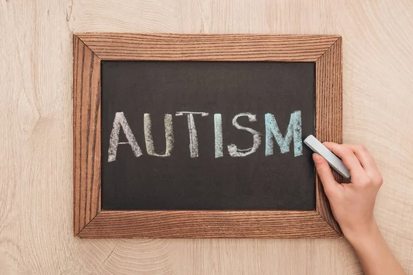 Vista parcial de la mujer escribiendo letras de autismo con tiza en pizarra - foto de stock