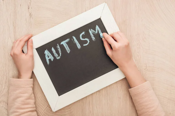 Teilansicht einer Frau, die mit blauer Kreide Autismus-Schriftzug auf Kreide schreibt — Stockfoto