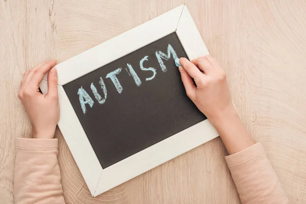 Vista parcial de la mujer escribiendo letras de autismo con tiza azul en pizarra - foto de stock