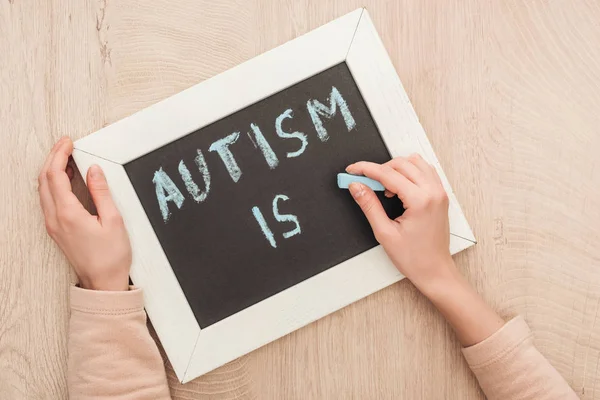 Vista parcial de la mujer escribiendo autismo está escribiendo con tiza azul en pizarra - foto de stock